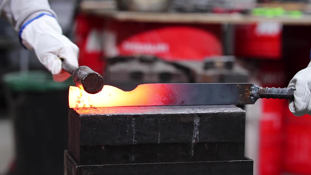 Blacksmiths forging hot metal with hammer in workshop
