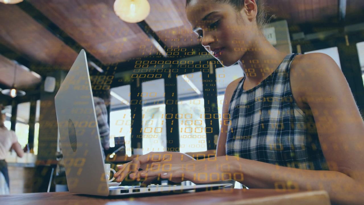 Frau tippt im Café auf Laptop, während die Kamera zurückfährt; binäre Überlagerung hebt technische Arbeit hervor.