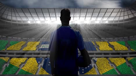 Animation-of-rear-view-of-football-player-holding-ball-over-brazilian-flag-in-sports-stadium