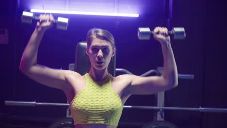 woman performing shoulder press with dumbbells in gym