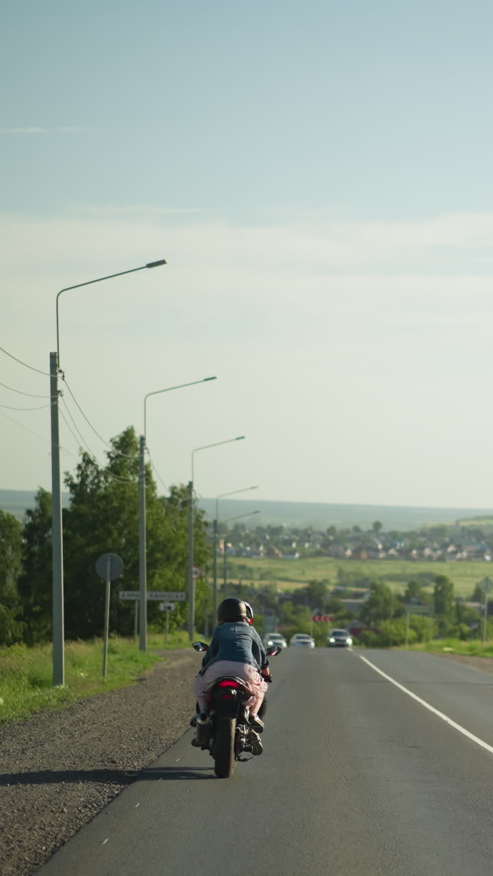 두 친구가 열려있는 도로에서 느린 속도로 전력 자전거를 타고있는 뒷면, 반대 방향에서 오는 자동차가 보이고, 나무의 경치 좋은 배경과 먼 주거 지역