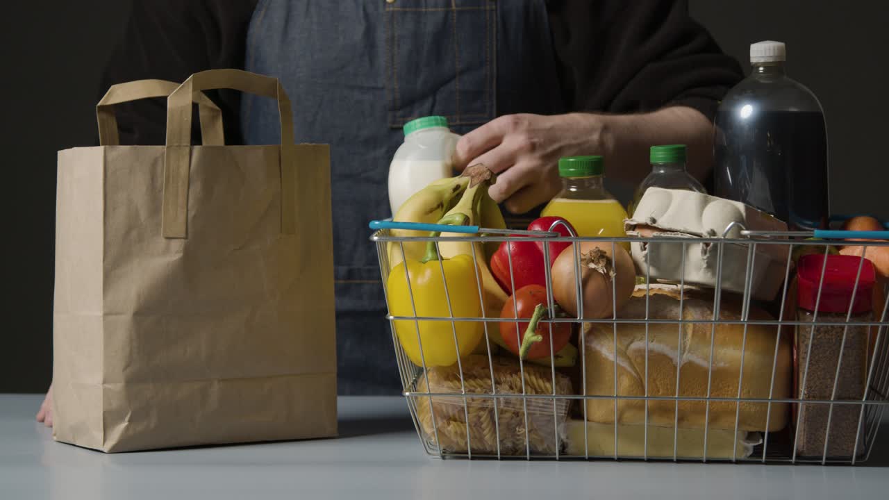 foto de estudio de un trabajador de la tienda empacando alimentos básicos en una cesta de compras de alambre de supermercado en una bolsa de papel