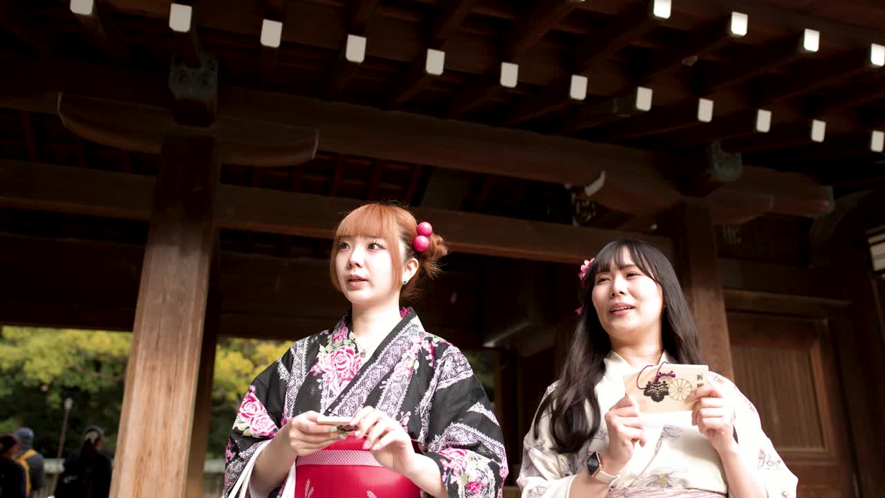 Due donne in kimono tradizionali tengono tavolette votive (ema) in legno mentre esplorano un santuario storico giapponese.