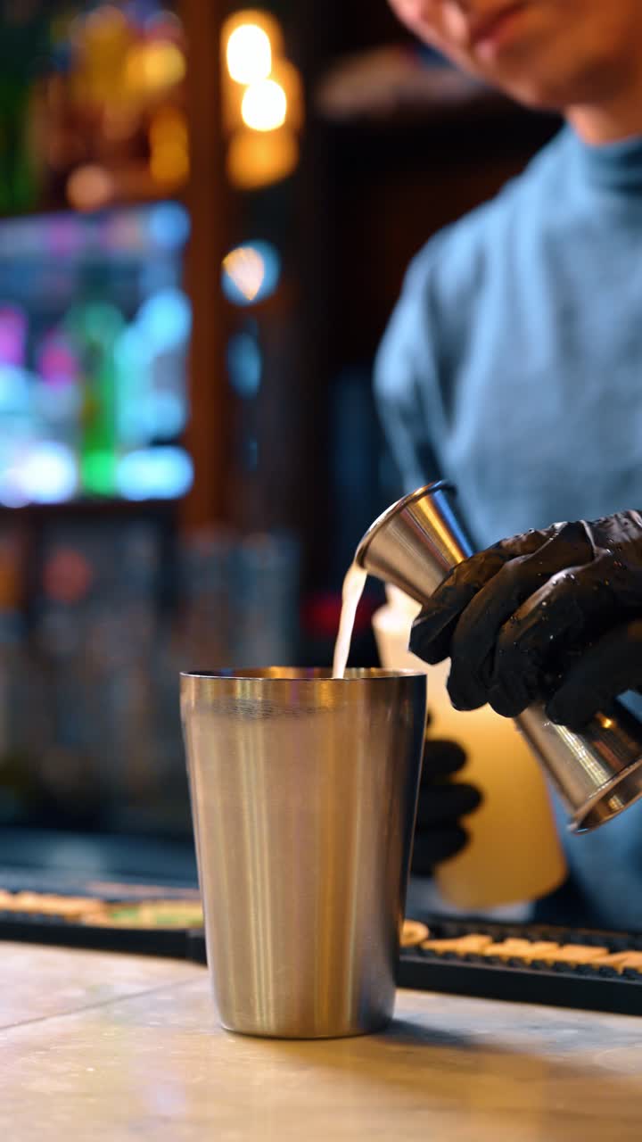 Barman che versa un ingrediente bianco da una bottiglia di plastica nello shaker. Scatto d'azione delle mani di un barman che versa liquido bianco da una bottiglia a spremere in uno shaker di metallo in un bar.
