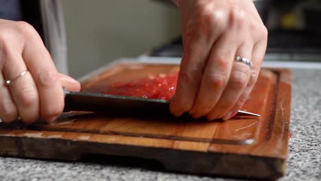 chef's hand chopping quickly red tomatoes using knife on wooden board