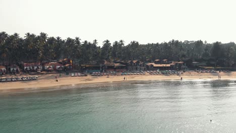 beach chairs resting in palolem beach near turquoise ocean shore - aerial low angle orbit panoramic shot