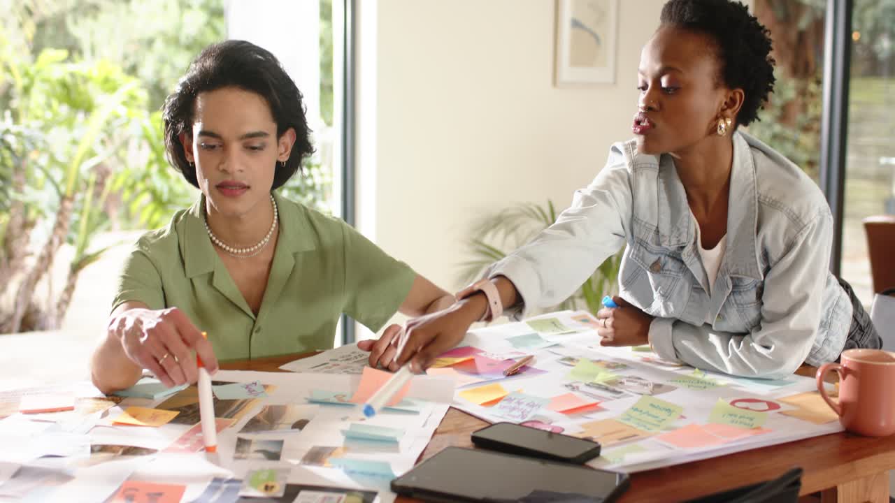 Diverse coworkers gesturing, arranging sticky notes, highlighting diagrams with highlighter at desk