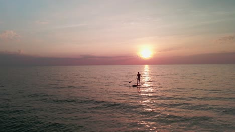 Drohnenaufnahme-Aus-Niedrigem-Winkel-Von-Mann-Stand-Up-Paddle-Boarding-Goldenes-Sonnenlicht-Der-Sonne,-Die-Am-Abend-Absteigt