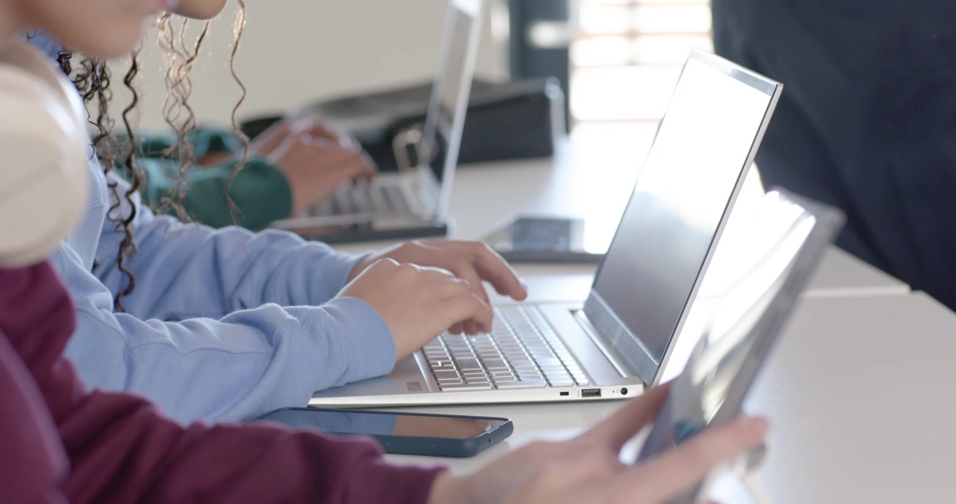 Teen peers tapping tablet typing laptop checking smartphone while camera panning in lab for study