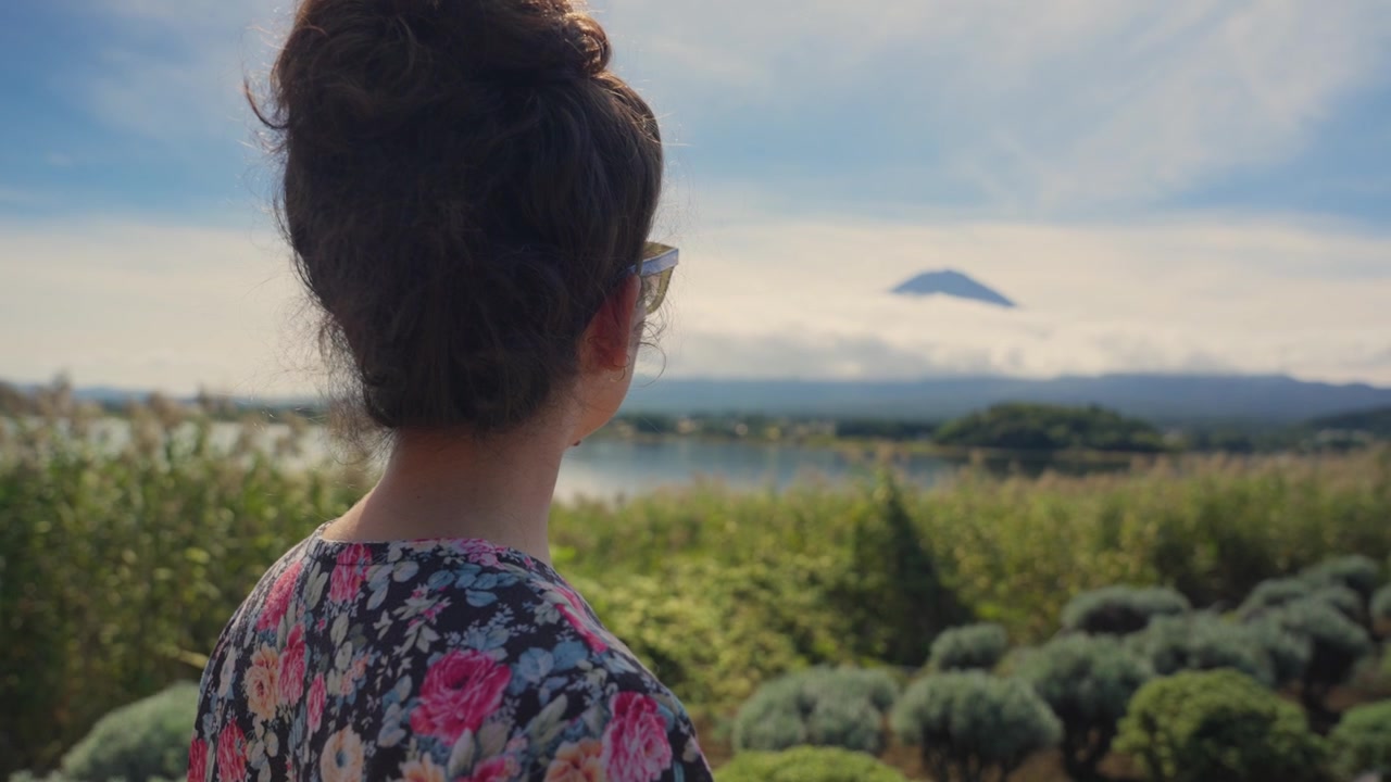 Young woman with her hair in a bun contemplating the stunning landscape of Mount Fuji and Lake Kawaguchiko in Japan, a beautiful and popular travel destination for its natural beauty
