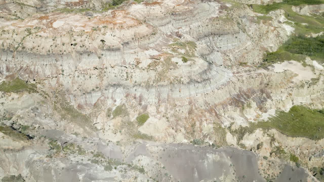 Aerial view of the Canadian Badlands showing sedimentary rock layers, eroded hills, and open grasslands under a bright sky. Canada - Canada