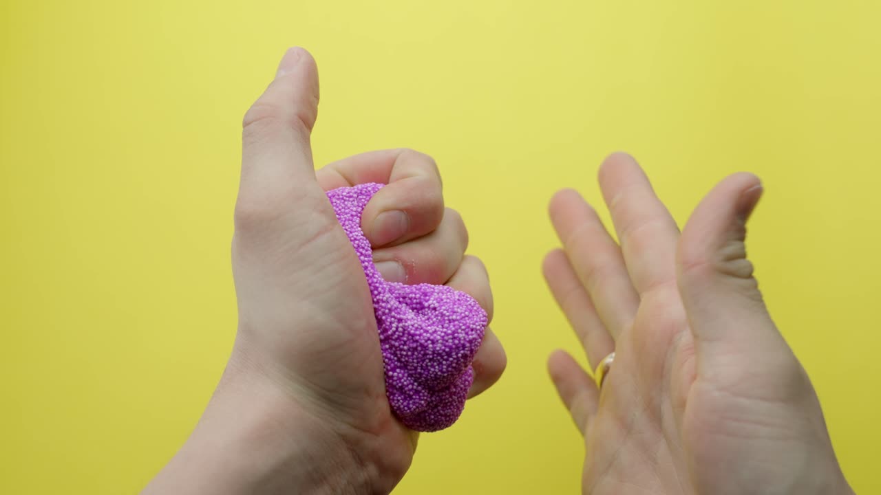 Close-up of hands squeezing and shaping purple floam slime on a bright yellow background, highlighting sensory play and tactile stress relief, demonstrating the texture and malleability, static shot