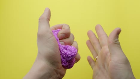 close-up of hands squeezing and shaping purple floam slime on a bright yellow background, highlighting sensory play and tactile stress relief, demonstrating the texture and malleability, static shot