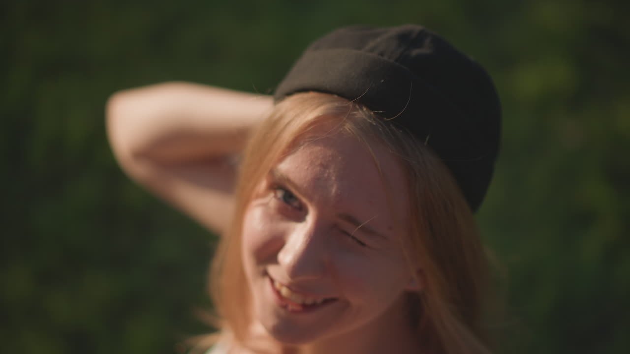 Iloinen nuori ulkoilija tekee iloisia eleitä, iloinen tyttö musta hattu päässä pitää hauskaa vihreässä puistossa, riemukas teinityttö auringonpaisteessa tekee leikkisiä eleitä aurinkoisena päivänä ulkona