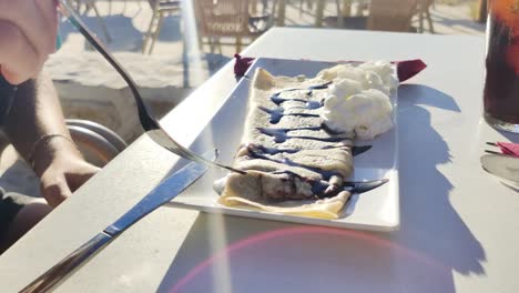 woman's hands cutting a crepe with syrup in