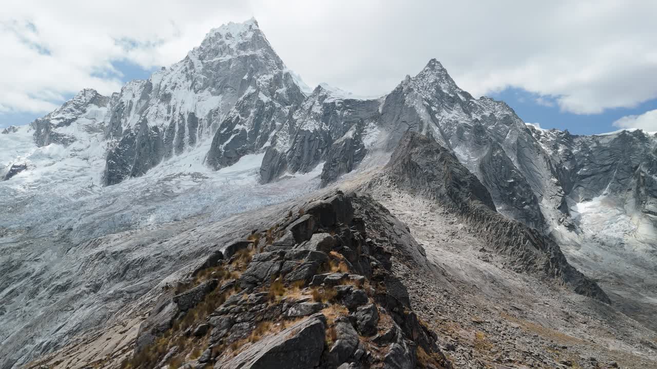 Spectacular aerial forward shot flies along a dramatic ridge near Punta Union Pass, with the iconic Taulliraju peak towering in the background on the Santa Cruz trek, Peru