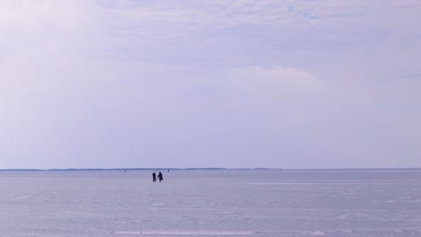 Two-fisher-men-walking-on-frozen-lake,-winter,-ice-fishing,-wide-landscape,-wide-shot