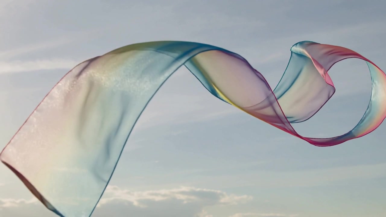 Drifting from light breeze, multicolored ribbon twisting across sunlit open sky with low cloud bank
