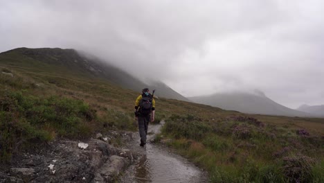 mann mit gelber jacke, der durch einen nebligen isle of skye trail wandert