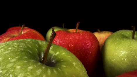 vista macro moviéndose hacia atrás sobre manzanas rojas y verdes frescas sobre fondo negro, fruta con gotas de agua