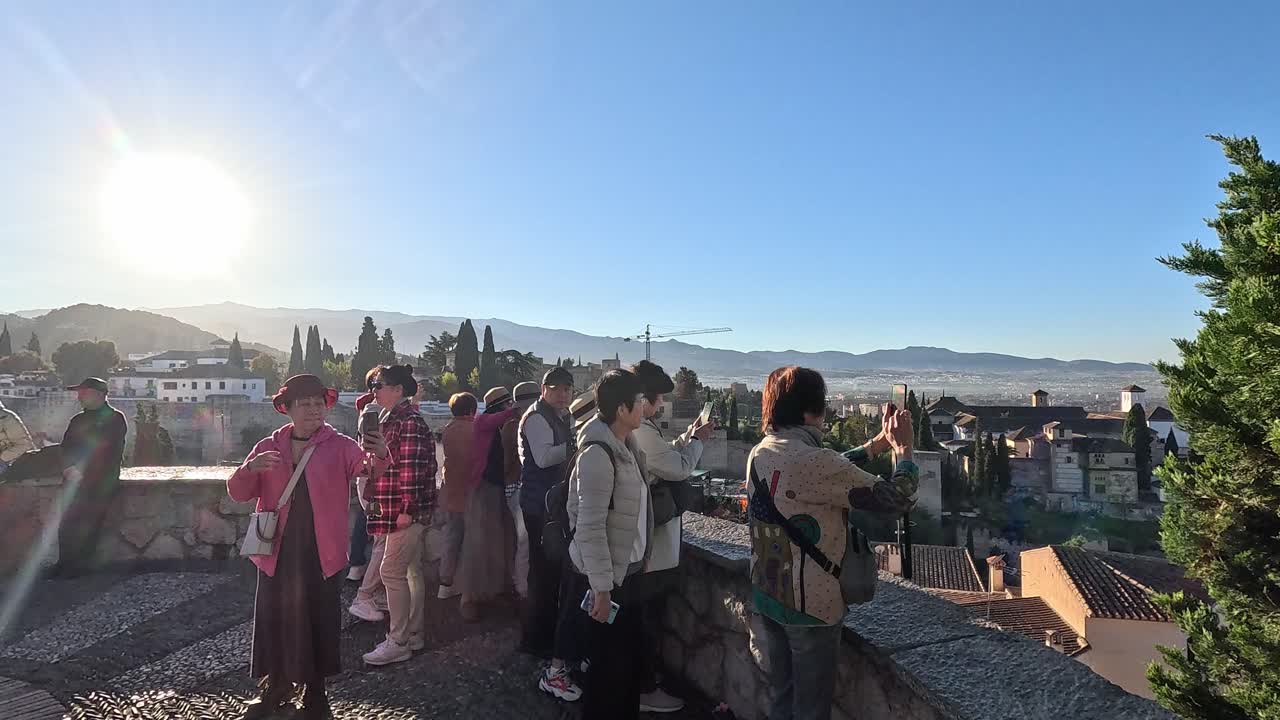 Evening light casts a warm glow over the Albaicin. Asian Tourist taking photos at the Mirado San Cristobal historic charm of this Granada neighborhood. Granada, Spain