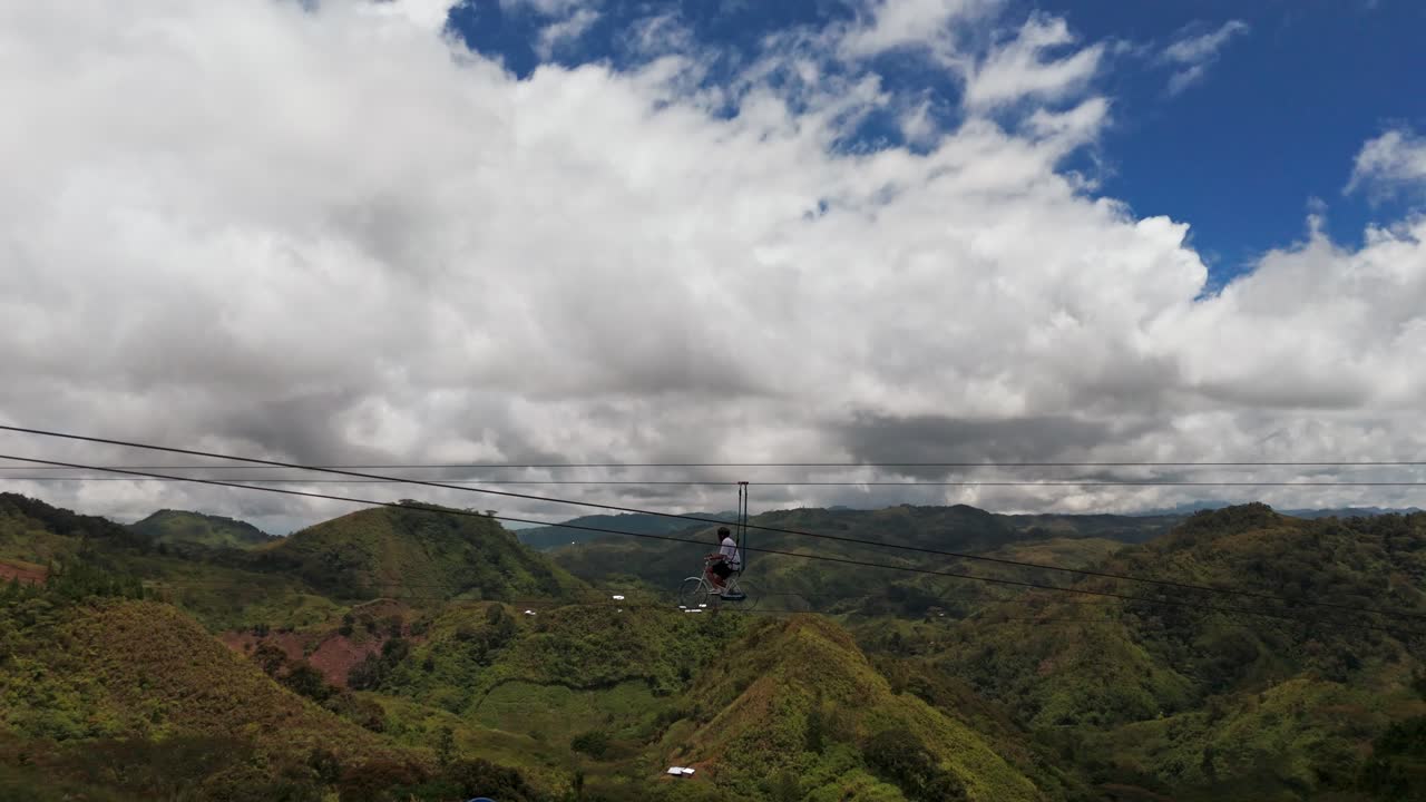 Cinematic 4K drone shot of a tourist riding a sky bike suspended above lush green mountains under dramatic clouds in the Philippines, perfect for travel, adventure, and tourism projects