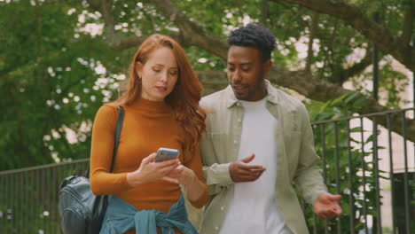 Pareja-Joven-Viajando-Juntos-Por-La-Ciudad-Siguiendo-Instrucciones-En-La-Aplicación-De-Mapas-En-El-Teléfono-Móvil