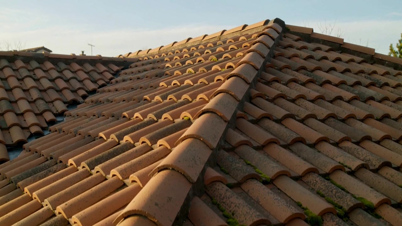 Telecamera che si allontana rivelando il colmo del tetto in terracotta su un tetto di casa, mettendo in risalto le chiazze di muschio