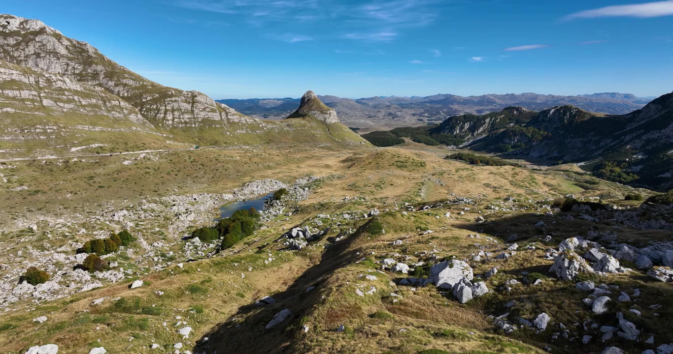 Panoramica aerea all'indietro di un vasto paesaggio montano aspro in una giornata di sole