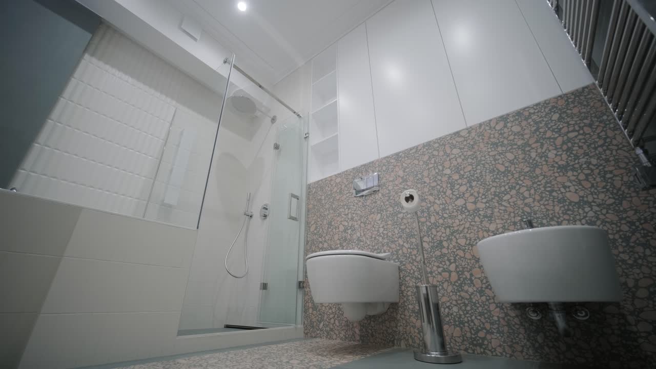 un baño contemporáneo cuenta con una amplia ducha con azulejos blancos, una pared de acento de terrazo única y accesorios minimalistas, creando una atmósfera elegante y serena