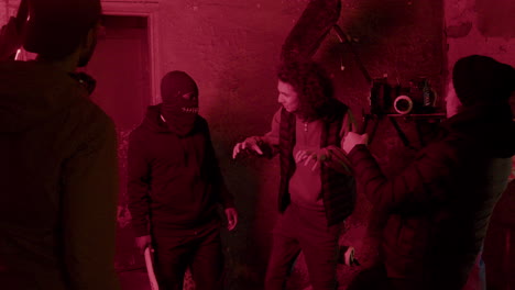 cameraman and production worker giving instructions to an man in black balaclava for a movie scene in a ruined building