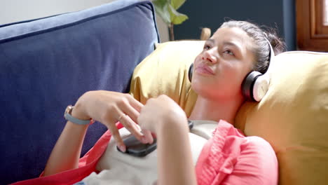 una adolescente biracial feliz con auriculares en el sofá escuchando música con su teléfono inteligente, en cámara lenta