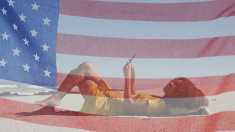 Animación-De-La-Bandera-Estadounidense-Ondeando-Sobre-Una-Mujer-Usando-Una-Tableta-Tumbada-En-La-Playa.