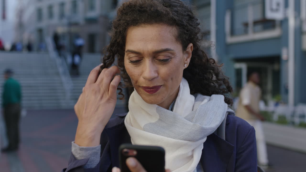 портрет в замедленном движении красивой женщины смешанной расы, отправляющей текстовые сообщения, просматривающей с помощью смартфона приложение социальных сетей, ожидающее в городе