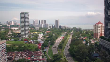 stunning drone footage showcasing a busy highway winding through the vibrant greenery and modern skyline of george town, penang, malaysia, highlighting urban development amidst nature.