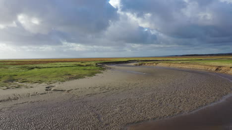 Low-drone-shot-of-large-flat-area-on-the-coat-of-England,-showing-the-rivers-of-the-tidal-waters