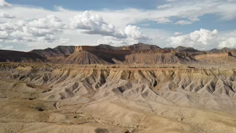 A-spectacular-4K-drone-shot-over-the-barren,-desert-hills-of-Grand-Valley-OHV-area,-with-the-steep-sloped-plateaus-of-the-Little-Book-Cliffs-in-the-distance,-located-in-Grand-Junction,-Colorado