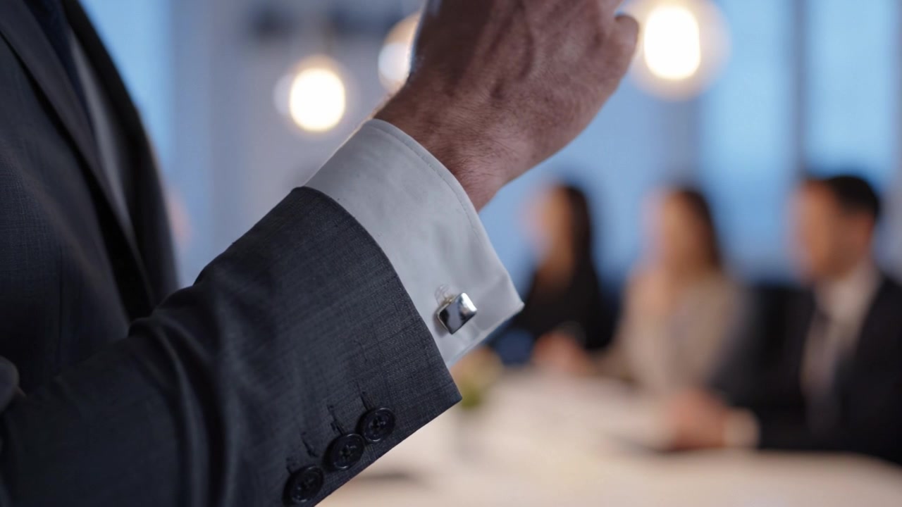 Una scena di riunione d'affari professionale con partecipanti impegnati in una discussione, focalizzata sul gesto del braccio di un individuo in abito per enfasi e coinvolgimento.