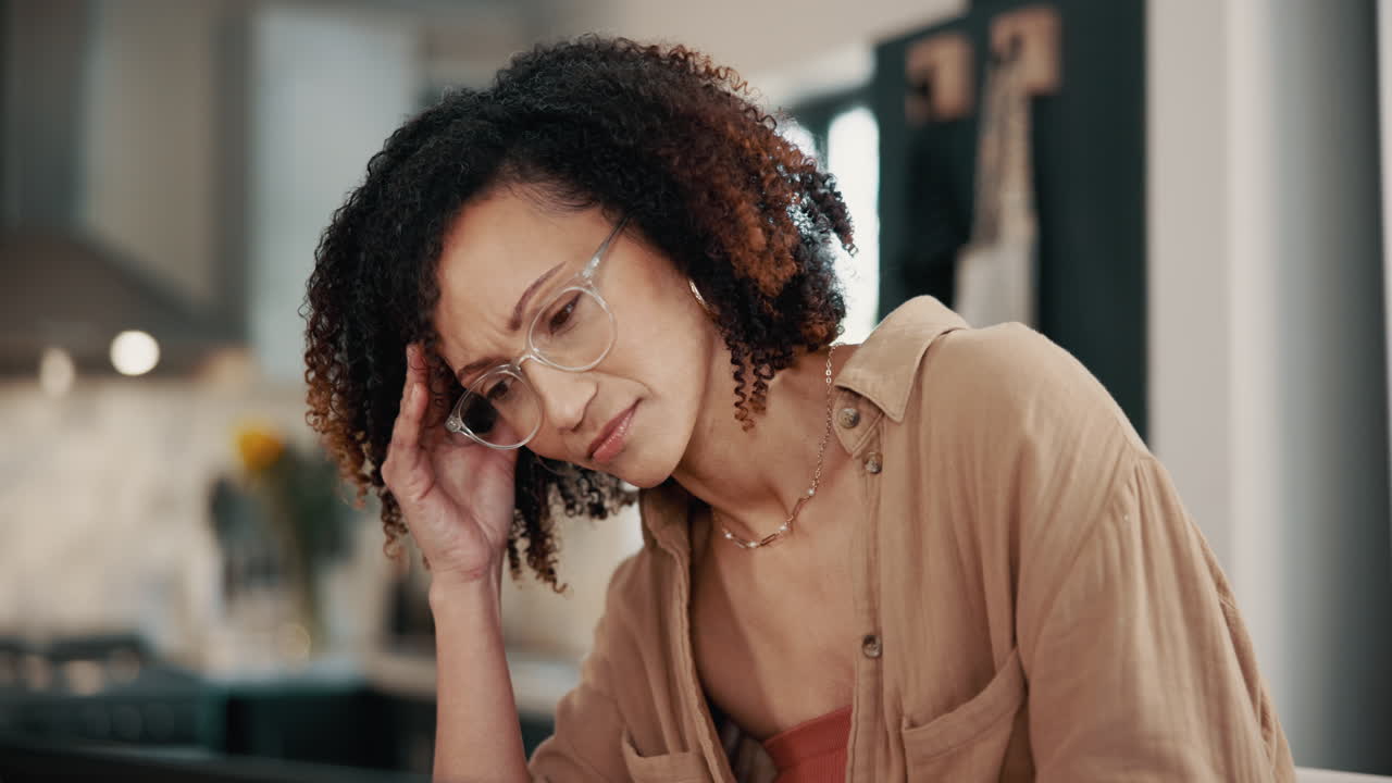 Woman with curly hair and glasses looking down thoughtfully