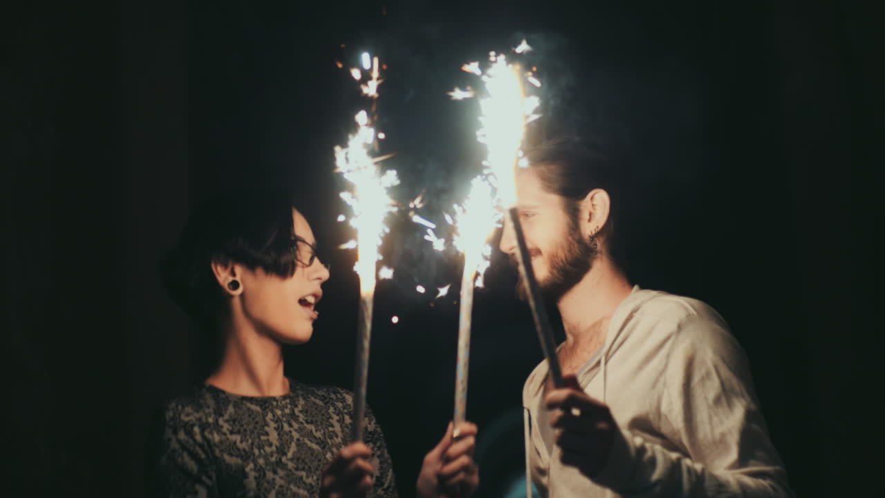 un joven con barba y una mujer morena divirtiéndose con fuegos artificiales en manos de