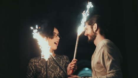 a young man with a beard and a brunette woman having fun with fireworks in the hands of