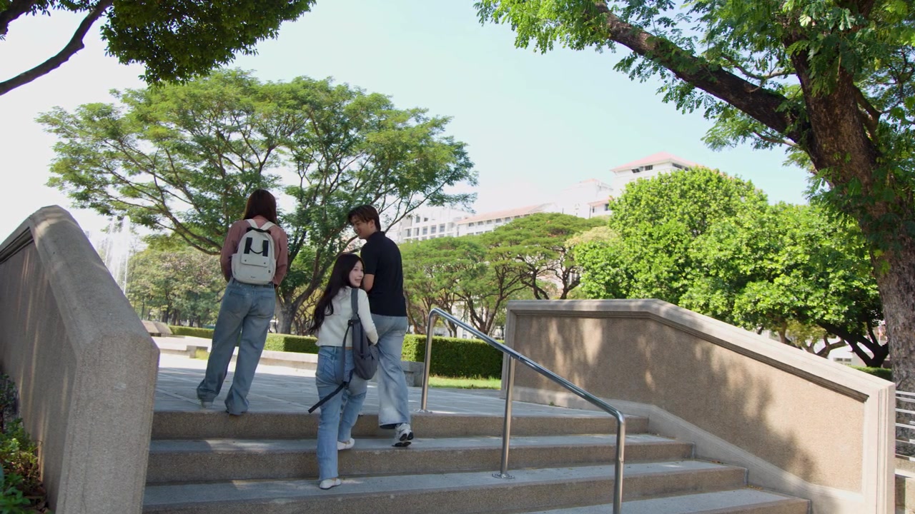 Tre studenti con gli zaini salgono scale di cemento in un soleggiato parco del campus universitario.