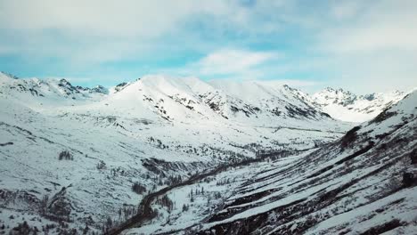 Flying-in-a-winter-valley-with-road-and-creek-below