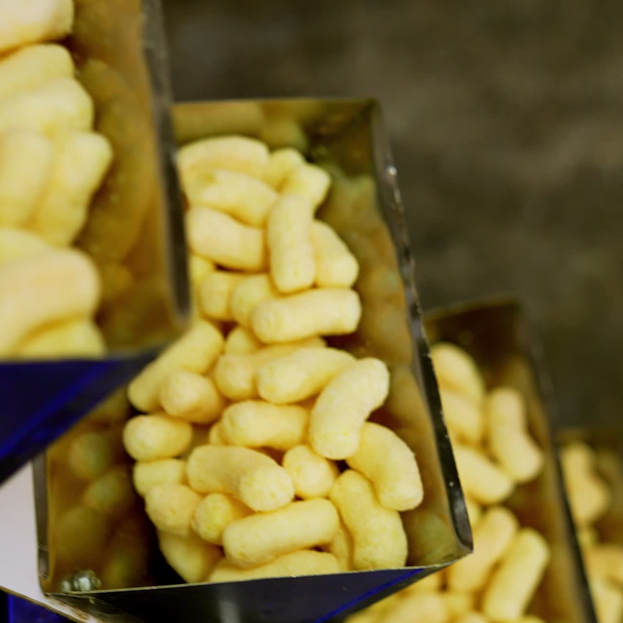 Automated process of sweet snacks production at food factory. Yellow corn sticks at conveyor belt. Close up