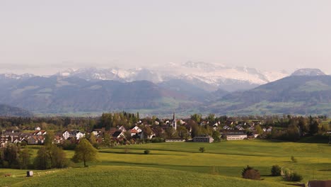 Drone-flies-over-a-hilly-landscape-in-spring-towards-a-village-with-a-church-in-the-center