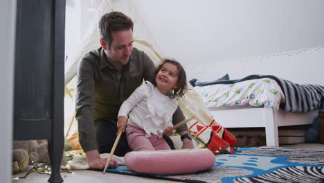 Single-Father-Playing-With-Daughter-Who-Drums-On-Cushion-In-Bedroom