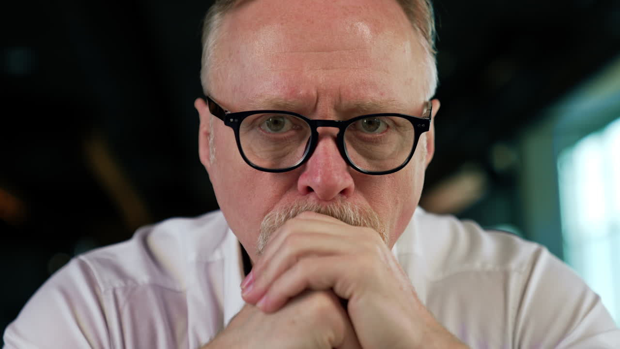 Mature Caucasian man thinking over the work issues. Businessman having trouble at work, sits looking at camera. Close up.