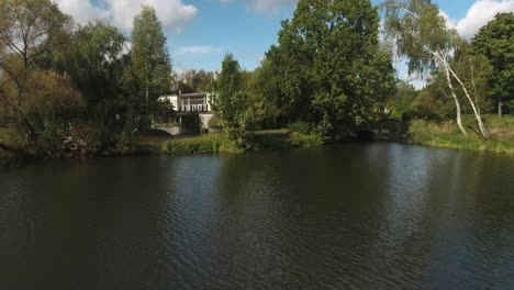 A-lake-in-an-urban-park-filled-with-greenery-and-trees,-with-a-restaurant-in-the-background-in-Poland-during-the-summer