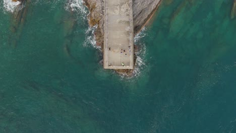 People-on-a-pier-in-genoa,-italy,-surrounded-by-the-clear-blue-waters-of-the-mediterranean,-aerial-view