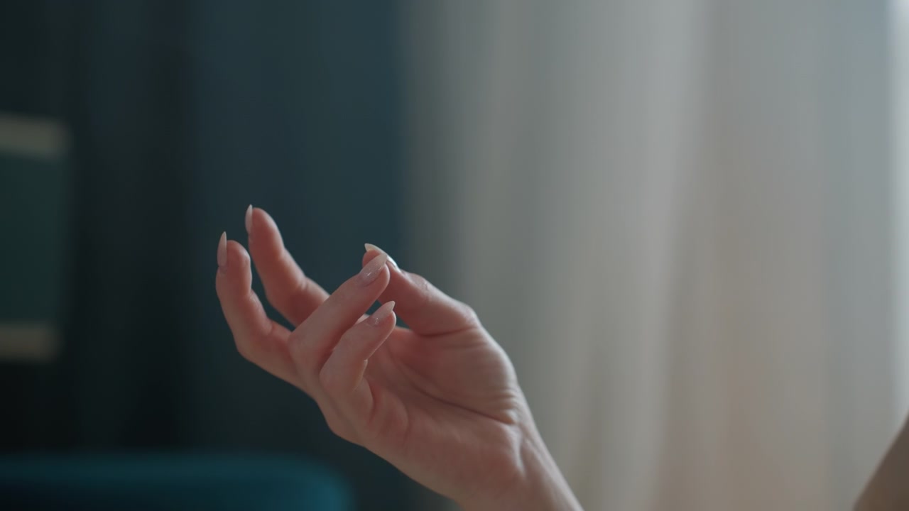 Dimly lit hand gesture near window, expressive sign used by grammar coach during online lesson, teal sofa backdrop, intimate study vibe, focus on fingers, subtle movement and breath pacing